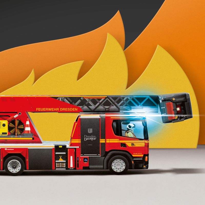 Bild zeigt zusammengestecktes Feuerwehrfahrzeug aus einem Faltfixx Bastelbogen, dieses steht vor künstlich erzeugten Flammensimulation