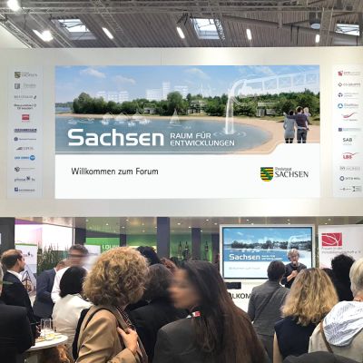 Der Messeauftritt des Freistaates Sachsen auf der EXPO Real 2019. Zu sehen ist unser Messemotiv auf dem Display der Frontseite des Messestandes.