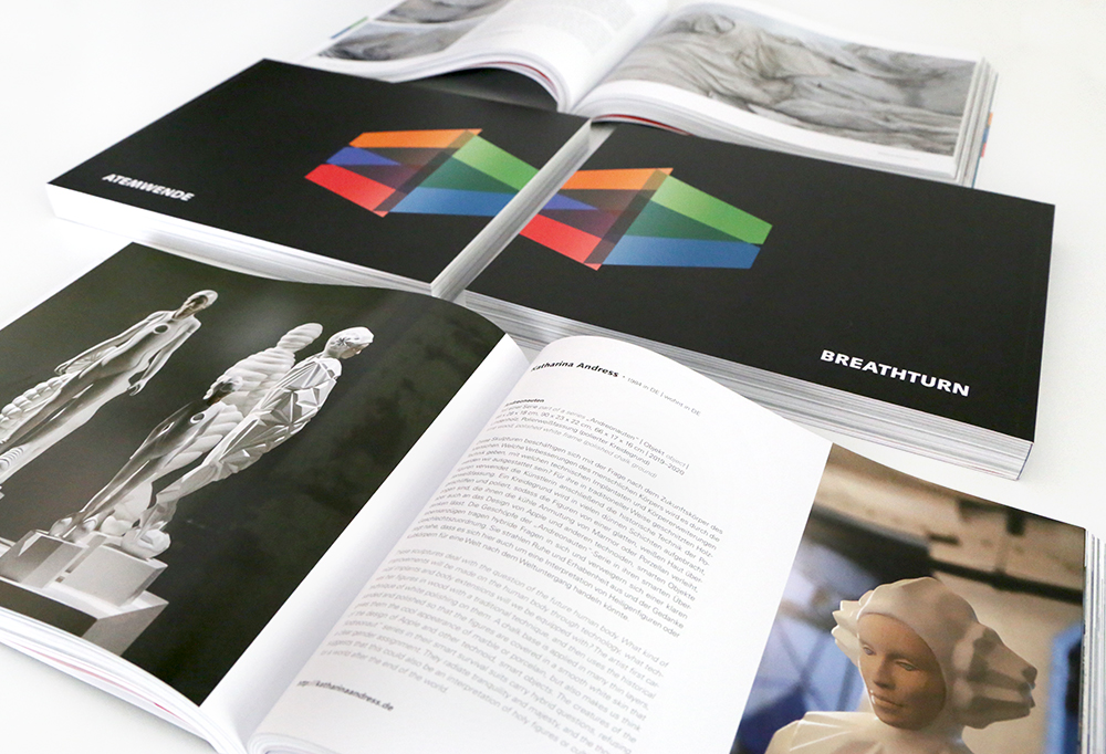 Foto: Der diesjährige Katalog in deutscher und englischer Sprache. Abgebildet ist der Titel in beiden Sprachen. Oberhalb und unterhalb der Titel sind Beispielseiten mit Kunstwerken aufgeschlagen.