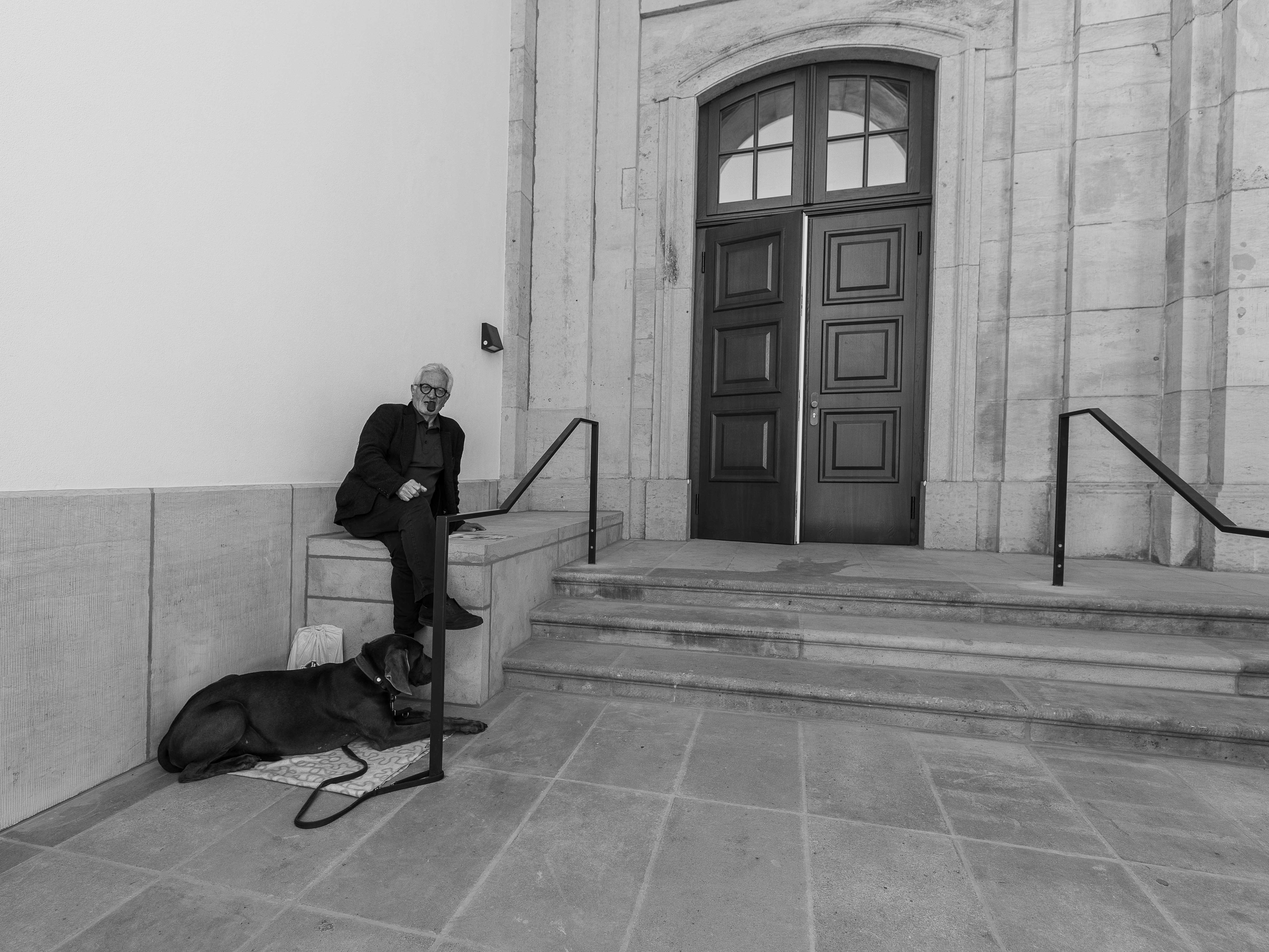 Mann mit Pfeife und Hund sitzt an den Stufen zum Eingang des historischen Blockhauses - C: Christoph Reichelt